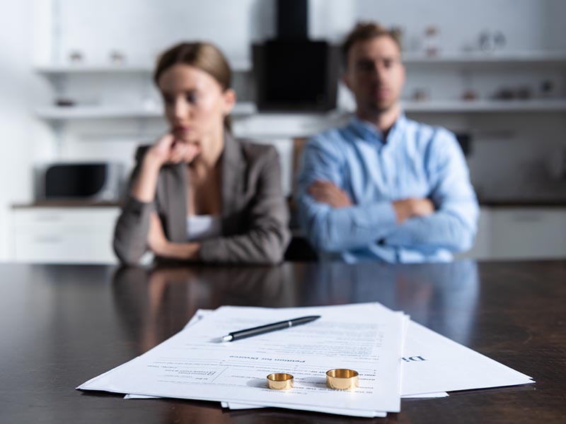 Man and woman sitting next to each other at table with divorce papers on top